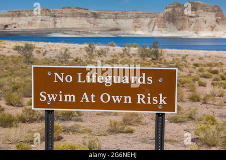 Ein braunes Schild mit weißem Schriftzug, auf dem steht, dass kein Rettungsschwimmer im Einsatz ist und dass Sie auf eigenes Risiko in dieser Gegend von Lake Powell in der Nähe schwimmen werden Stockfoto