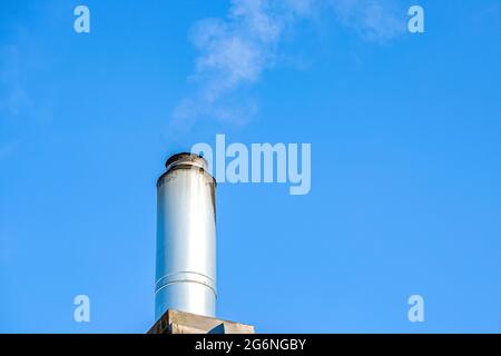 Kamin mit aufsteigendem Rauch am blauen Himmel. Heizung des Hauses im Winter. Edelstahlkamin mit aufsteigendem Rauch Stockfoto