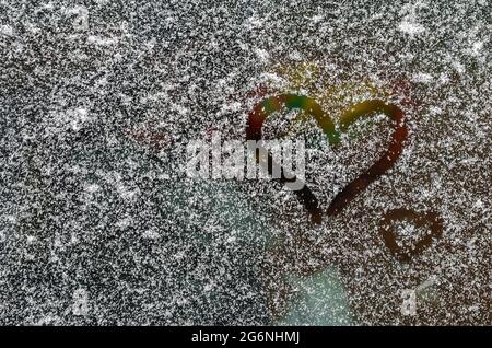 Ein von den Fingern gezogenes Herz auf einer schneebedeckten Windschutzscheibe. LGBT. Valentinstag-Konzept. Valentinstag kreativer Hintergrund. Stockfoto