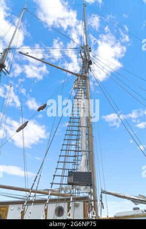 Holzmast und Seile des Segelbootes, Blick auf die Masten des Schiffes von unten, detailliertes Takelieren ohne Segel gegen den blauen Himmel mit weißen Wolken. Stockfoto