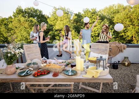 Junge, stilvolle Freunde bei einem festlichen Abendessen auf der Dachterrasse Stockfoto