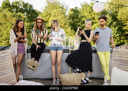 Menschen verbringen Zeit miteinander, sitzen getrennt in Smartphones auf Party im Freien Stockfoto