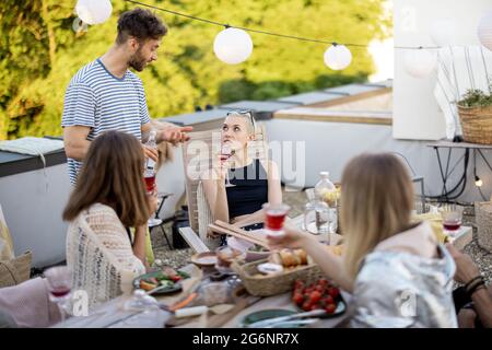 Junge, stilvolle Freunde bei einem festlichen Abendessen auf der Dachterrasse Stockfoto