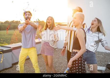 Junge, stilvolle Freunde feiern auf dem Dach bei Sonnenuntergang Stockfoto