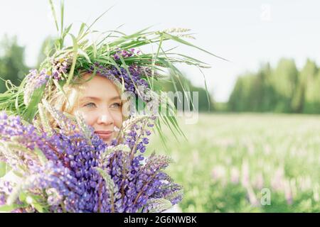 Ein hippes Mädchen, das einen Blumenstrauß in den Händen hält. Mädchen versteckte ihr Gesicht hinter einem Blumenstrauß aus Lupinen. Mädchen hält große Bouquet von lila Lupinen in einem Stockfoto