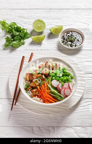 Tofu-Schüssel mit Basmati-Reis, edamamen Bohnen, Rettich, dünn geschnittener Gurke und Karotten in einer weißen Schüssel mit Essstäbchen, vertikale Ansicht von oben, Stockfoto