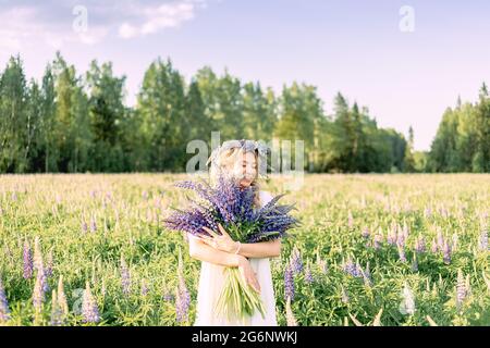 Ein hippes Mädchen, das einen Blumenstrauß in den Händen hält. Mädchen versteckte ihr Gesicht hinter einem Blumenstrauß aus Lupinen. Mädchen hält große Bouquet von lila Lupinen in einem Stockfoto