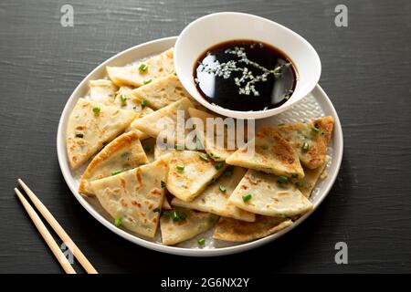 Hausgemachte Scallion-Pfannkuchen mit Soja-Dipping-Sauce auf schwarzer Oberfläche, Seitenansicht. Stockfoto