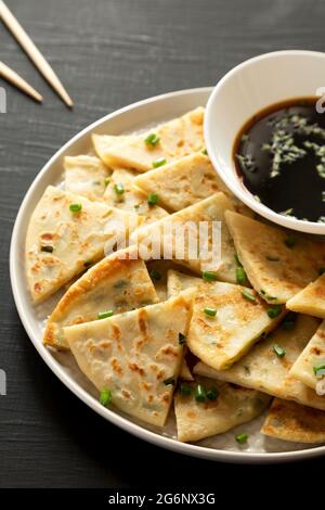 Hausgemachte Scallion-Pfannkuchen mit Soja-Dipping-Sauce auf schwarzem Hintergrund, Seitenansicht. Stockfoto