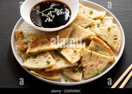 Hausgemachte Scallion-Pfannkuchen mit Soja-Dipping-Sauce auf schwarzer Oberfläche, Seitenansicht. Stockfoto