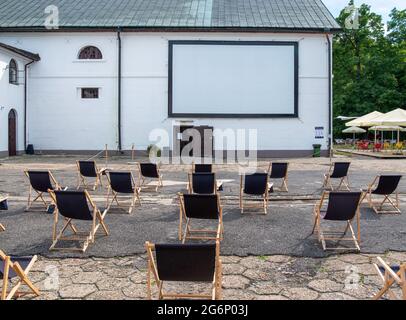 Oper-Air, Freiluftkino im Hof der Brauerei in Zwierzyniec, Polen. Reihen schlichter, schwarzer Sonnenliegen vor dem Bildschirm, die an der Wand angebracht sind. Stockfoto