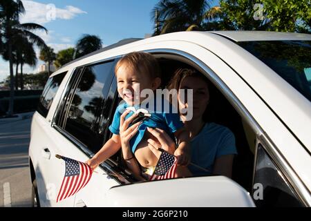 Ein Kleinkind winkt amerikanische Flaggen aus einem Autofenster Stockfoto