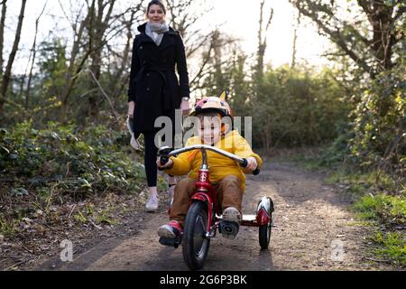 Ein kleines Kind, das mit seiner Mutter auf einem Dreirad reitet Stockfoto