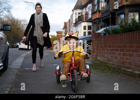 Ein kleines Kind, das mit seiner Mutter auf einem Dreirad reitet Stockfoto