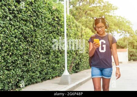 Teenager mit Kopfhörern, die das Telefon benutzen, während sie im Park spazieren gehen und Musik hören Stockfoto
