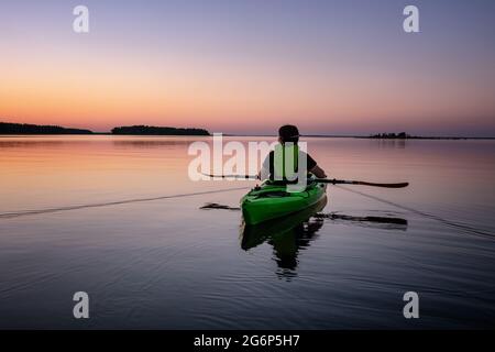 Kajakerinnen halten waagerecht Paddel, Seekajak um Mitternacht in Nordschweden während leichter Sommernächte. Spiegel wie Wasseroberfläche. Umea, Stockfoto