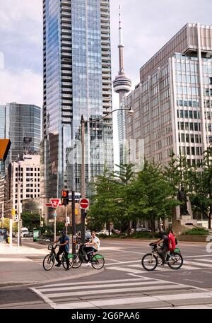 TORONTO, KANADA - 06 05 2021: Radfahrer auf der Queen Street an der Kreuzung der University Avenue in der Innenstadt von Toronto mit dem CN Tower, der zwischen Wolkenkratzern sichtbar ist Stockfoto