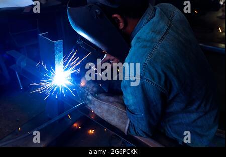 Schweißer schweißen Metall mit Argon-Lichtbogen-Schweißmaschine und hat Schweißfunken. Ein Mann trägt Schweißmaske und Schutzhandschuhe. Sicherheit in der Industrie Stockfoto