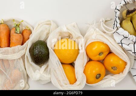 Frisches Obst, Gemüse in Öko-Baumwollbeuteln auf einem beigen Tisch. Karotten, Orangen, Bananen, Avocado vom Markt. Zero Waste Shopping-Konzept. Stockfoto