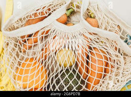 Frisches Gemüse in einem beigefarbenen wiederverwendbaren Baumwoll-Mesh-Beutel auf beigem Hintergrund. Umweltfreundliche Einkaufstasche. Zero Waste Lebensmittelkonzept. Nachhaltiges Leben Stockfoto