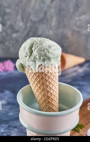 Pistazien-Eis in Waffelkegel und Vase auf blauem Hintergrund Stockfoto