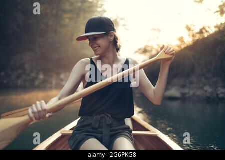 Junge Frau paddelt Kanu auf einem Waldsee Stockfoto