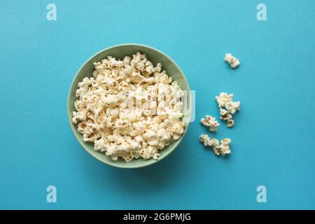 Popcorn in Keramikschale auf blauem Hintergrund. Draufsicht, flach liegend. Stockfoto