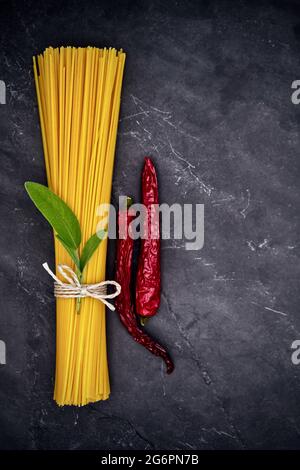 Pasta mit einem Band, einem Zweig aus Salbei und getrockneten Chilischoten auf einem schwarzen Schieferteller gebunden Stockfoto