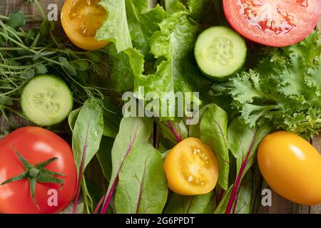 Draufsicht auf verschiedene Salatsorten und Gurken, rote und gelbe Tomaten. Junge saftige Sprossen aus Erbsen oder Bohnen, Rübensprossen und grünem Salat. Gesundes Lebensmittelkonzept. Flat Lay Soft Focus Stockfoto