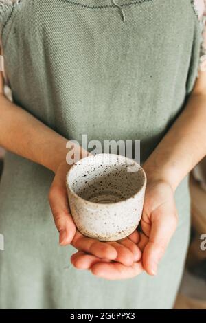 Eine Kunsthandwerkerin hält einen handgefertigten Keramikbecher in den Händen. Kleinunternehmen Stockfoto