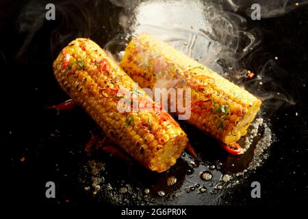 Von oben leckere gesunde Maiskolben, die in heißem Öl auf schwarzer Oberfläche vorbereiten Stockfoto