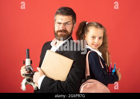 Grundschüler mit Lehrer im roten Studio, isoliert. Porträt von lustigen Schulmädchen und Tutor mit Schulbedarf. Glückliche Lehrerin und Schülerin Mädchen auf Stockfoto