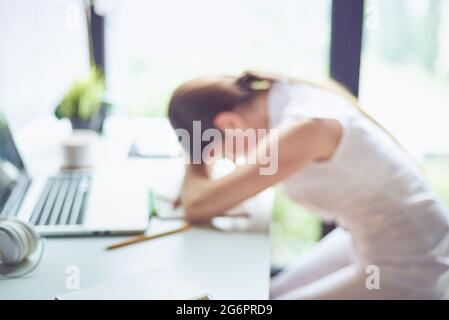 Defokussiertes Foto von gelangweilt überarbeiteten und frustrierten jungen Frau kreativen Profi an ihrem Arbeitsplatz schlafen über einem Laptop. Müde junge Frau fallin Stockfoto