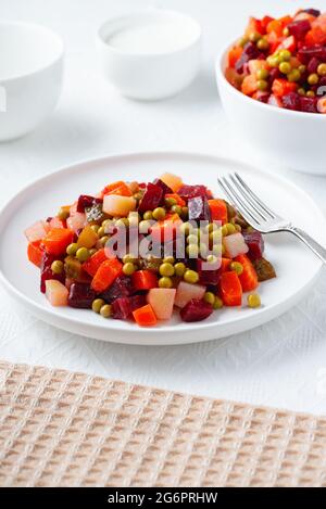 Traditionelle russische Salat-Vinaigrette mit gekochtem Gemüse, eingelegten Gurken und Sauerkraut in Teller auf weißem Tisch. Stockfoto