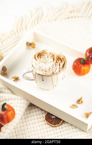 Kürbis-Latte mit Schlagsahne und Sirup auf einem weißen Tablett mit Karotte und kleinen Halloween-Kürbissen im Herbst. Stockfoto