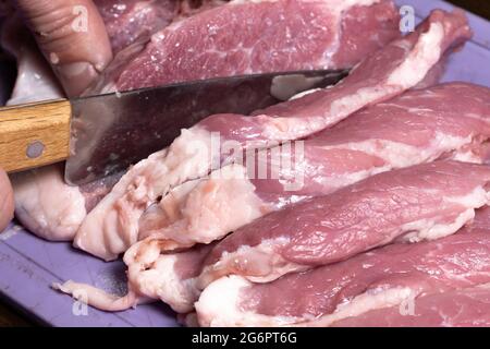 Schneiden Sie das Schwein oder Rindfleisch mit einem Messer in Nahaufnahme auf den Tisch.Zubereitung von Fleischgerichten und Lebensmittelprodukten.Stücke von rotem Fleisch für den Schischkebab, Grill Stockfoto