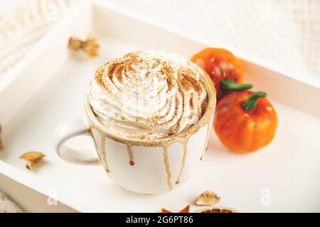 Kürbis-Latte mit Schlagsahne und Sirup auf einem weißen Tablett mit Karotte und kleinen Halloween-Kürbissen im Herbst. Stockfoto