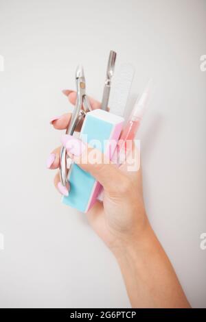 Vertikale Nahaufnahme von Maniküre-Instrumenten in weiblicher Hand mit rosa Nägeln Stockfoto