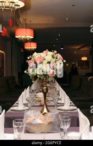 Wunderschön servierte Tafel in einem Restaurant mit einem Bouquet aus weißen und rosafarbenen Blumen in einer goldenen Vase Stockfoto