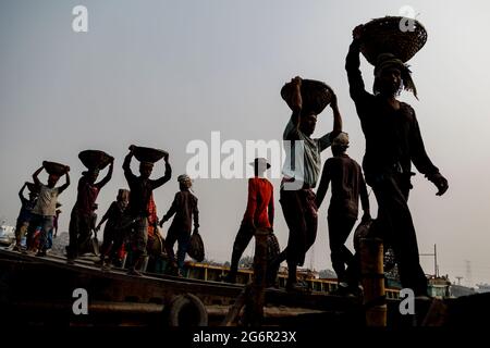 Eine menschliche Kette von Trägern trägt Kohle, Sand und Kies von den Bargen, die an der Aminbazar Landing Station am Buriganga River außerhalb von Dhaka festgemacht sind. Bangladesch absolviert derzeit den Abschluss der LDC-Kategorie (am wenigsten entwickelte Länder), was zum großen Teil der extrem harten Arbeit billiger Arbeitskräfte zu verdanken ist. Ein Portier macht zwischen 80 und 140 USD pro Monat, laut den Websites paylab.com und averagesalarysurvey.com Stockfoto