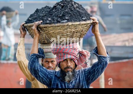 Eine menschliche Kette von Trägern trägt Kohle, Sand und Kies von den Bargen, die an der Aminbazar Landing Station am Buriganga River außerhalb von Dhaka festgemacht sind. Bangladesch absolviert derzeit den Abschluss der LDC-Kategorie (am wenigsten entwickelte Länder), was zum großen Teil der extrem harten Arbeit billiger Arbeitskräfte zu verdanken ist. Ein Portier macht zwischen 80 und 140 USD pro Monat, laut den Websites paylab.com und averagesalarysurvey.com Stockfoto