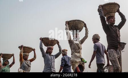 Eine menschliche Kette von Trägern trägt Kohle, Sand und Kies von den Bargen, die an der Aminbazar Landing Station am Buriganga River außerhalb von Dhaka festgemacht sind. Bangladesch absolviert derzeit den Abschluss der LDC-Kategorie (am wenigsten entwickelte Länder), was zum großen Teil der extrem harten Arbeit billiger Arbeitskräfte zu verdanken ist. Ein Portier macht zwischen 80 und 140 USD pro Monat, laut den Websites paylab.com und averagesalarysurvey.com Stockfoto