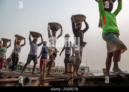 Eine menschliche Kette von Trägern trägt Kohle, Sand und Kies von den Bargen, die an der Aminbazar Landing Station am Buriganga River außerhalb von Dhaka festgemacht sind. Bangladesch absolviert derzeit den Abschluss der LDC-Kategorie (am wenigsten entwickelte Länder), was zum großen Teil der extrem harten Arbeit billiger Arbeitskräfte zu verdanken ist. Ein Portier macht zwischen 80 und 140 USD pro Monat, laut den Websites paylab.com und averagesalarysurvey.com Stockfoto