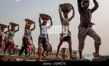 Eine menschliche Kette von Trägern trägt Kohle, Sand und Kies von den Bargen, die an der Aminbazar Landing Station am Buriganga River außerhalb von Dhaka festgemacht sind. Bangladesch absolviert derzeit den Abschluss der LDC-Kategorie (am wenigsten entwickelte Länder), was zum großen Teil der extrem harten Arbeit billiger Arbeitskräfte zu verdanken ist. Ein Portier macht zwischen 80 und 140 USD pro Monat, laut den Websites paylab.com und averagesalarysurvey.com Stockfoto