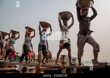 Eine menschliche Kette von Trägern trägt Kohle, Sand und Kies von den Bargen, die an der Aminbazar Landing Station am Buriganga River außerhalb von Dhaka festgemacht sind. Bangladesch absolviert derzeit den Abschluss der LDC-Kategorie (am wenigsten entwickelte Länder), was zum großen Teil der extrem harten Arbeit billiger Arbeitskräfte zu verdanken ist. Ein Portier macht zwischen 80 und 140 USD pro Monat, laut den Websites paylab.com und averagesalarysurvey.com Stockfoto