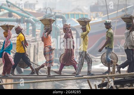 Eine menschliche Kette von Trägern trägt Kohle, Sand und Kies von den Bargen, die an der Aminbazar Landing Station am Buriganga River außerhalb von Dhaka festgemacht sind. Bangladesch absolviert derzeit den Abschluss der LDC-Kategorie (am wenigsten entwickelte Länder), was zum großen Teil der extrem harten Arbeit billiger Arbeitskräfte zu verdanken ist. Ein Portier macht zwischen 80 und 140 USD pro Monat, laut den Websites paylab.com und averagesalarysurvey.com Stockfoto