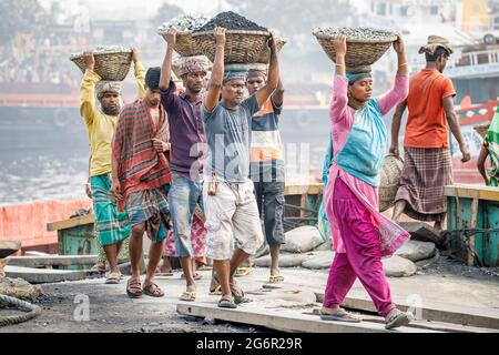 Eine menschliche Kette von Trägern trägt Kohle, Sand und Kies von den Bargen, die an der Aminbazar Landing Station am Buriganga River außerhalb von Dhaka festgemacht sind. Bangladesch absolviert derzeit den Abschluss der LDC-Kategorie (am wenigsten entwickelte Länder), was zum großen Teil der extrem harten Arbeit billiger Arbeitskräfte zu verdanken ist. Ein Portier macht zwischen 80 und 140 USD pro Monat, laut den Websites paylab.com und averagesalarysurvey.com Stockfoto