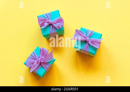 Drei türkise Geschenk-Boxen mit Schleife auf gelbem Hintergrund. Draufsicht, flach liegend. Stockfoto