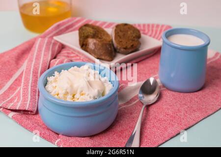 Quark in einer blauen Schüssel mit Sauerrahm und Honig. Geröstetes Brot auf einem Teller. Frühstück am Morgen. Stockfoto