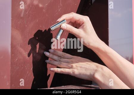 Lieferung der Batterien an die Recyclingstelle. Eine Frau hält zwei Batterien in der Hand und legt sie in einen Recyclingbehälter. Stockfoto